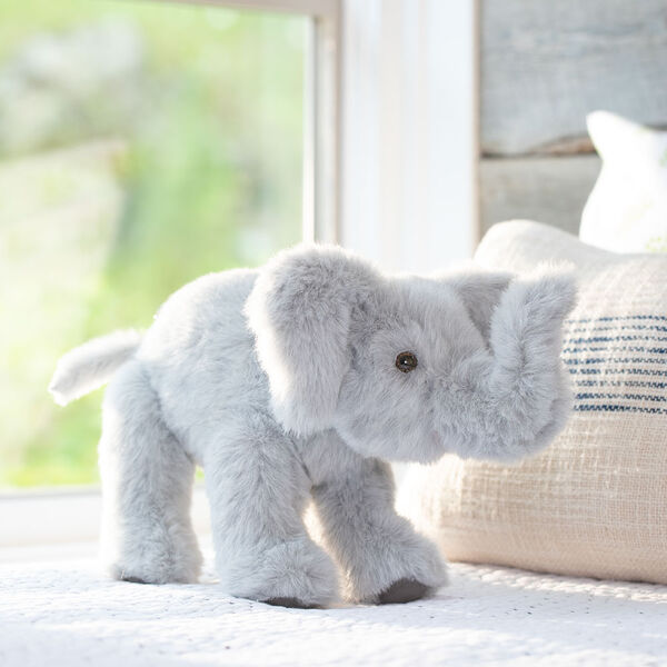 15" Classic Elephant - Side view of standing gray plush elephant with upturned trunk, gray foot pads and pink mouth in a bedroom scene.  image number 3