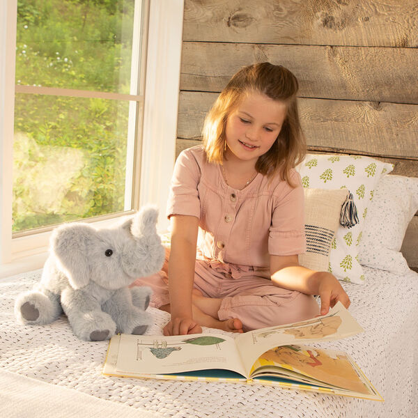 15" Classic Elephant - Three quarter view of seated gray plush elephant in a bedroom scene with a girl model image number 1