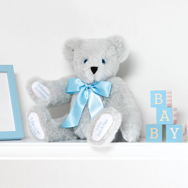 15" Premium Baby Boy Bear - Front view of seated jointed gray bear with white paw pads and chose of eye color wearing a blue satin bow in a bedroom scene.