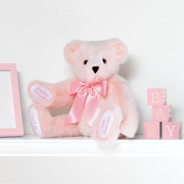 15" Premium Baby Girl Bear - Front view of seated jointed pink bear with white paw pads and chose of eye color wearing a blue satin bow in a bedroom scene. image number 1