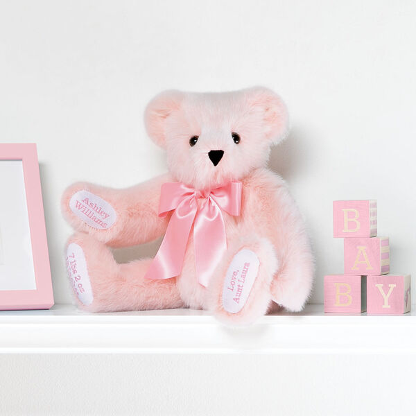 15" Premium Baby Girl Bear - Front view of seated jointed pink bear with white paw pads and chose of eye color wearing a blue satin bow in a bedroom scene.