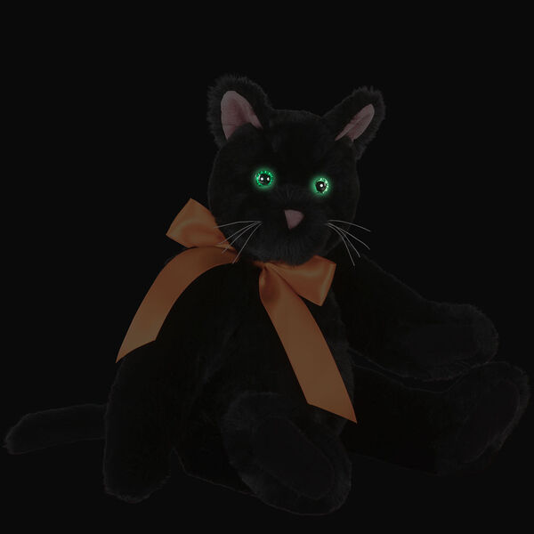 15" Classic Black Cat - Front view of seated jointed cat with pink ears, black foot pads and green eyes dressed in an orange satin bow in the dark showing the eyes glowing - Black fur image number 2