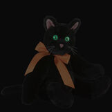 15" Classic Black Cat - Front view of seated jointed cat with pink ears, black foot pads and green eyes dressed in an orange satin bow in the dark showing the eyes glowing - Black fur image number 2