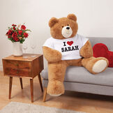 4' Big Hunka Love&reg; I HEART You T-Shirt Bear - Seated honey brown bear with white t-shirt personalized with "I Heart Sarah" in red and black graphics in living room scene image number 0