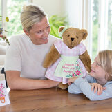 15" Home Is Where Your Mom Is Bear - Front view of standing jointed bear wearing a pink gingham dress, green bow and apron with floral embroidery and says "Home is Where Your Mom Is" with models image number 1