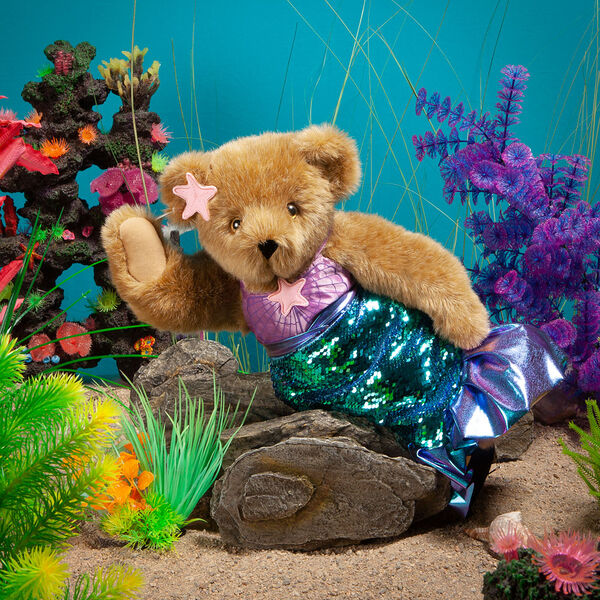 15" Mermaid Bear - Front view of standing jointed bear dressed in a blue sequin tail and purple top with shell embroidery an pink starfish applique and earpiece in an underwater scene - honey brown fur image number 1